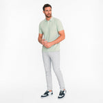 Man wearing a light green polo shirt and gray pants on a white background