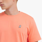 Close-up of a person wearing an orange t-shirt with a small logo on a white background