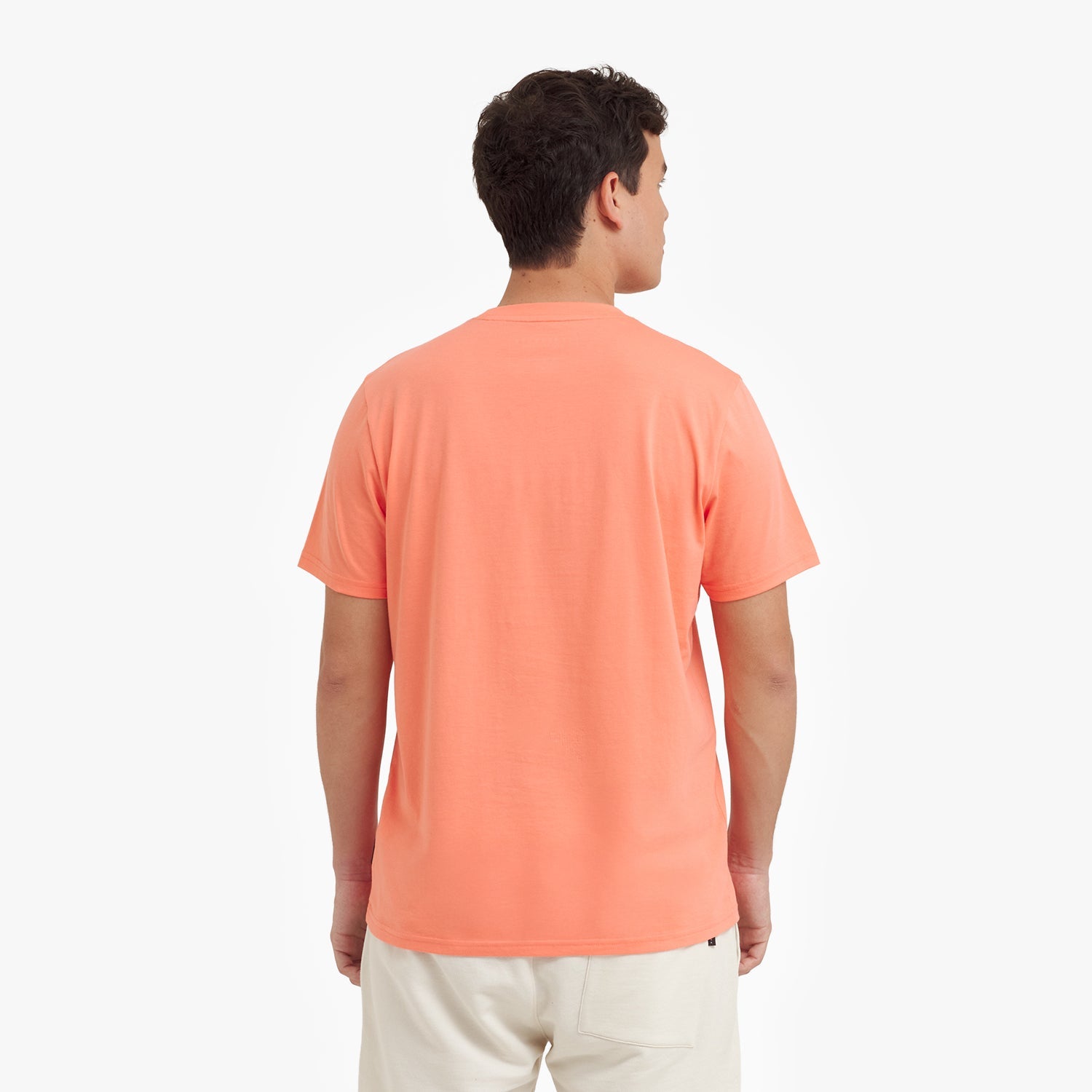 Back view of a man wearing a peach-colored t-shirt on a white background