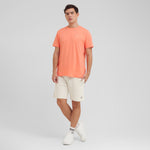 Man wearing an orange t-shirt and white shorts on a light gray background