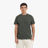 Man wearing a green t-shirt with a small logo on a white background
