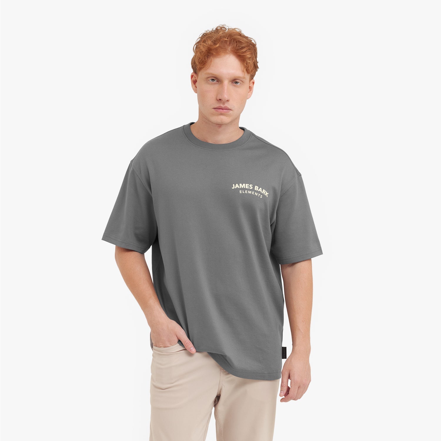 A male model with red hair wearing an oversized gray t-shirt and beige pants, looking at the camera