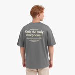 Back view of a male model wearing a gray t-shirt with a large "Seek the truly exceptional" graphic