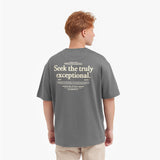 Back view of a male model wearing a gray t-shirt with a large "Seek the truly exceptional" graphic