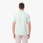 A man viewed from the back wearing a light mint green short-sleeve polo shirt and beige trousers