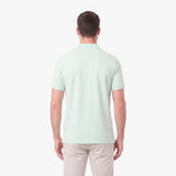 A man viewed from the back wearing a light mint green short-sleeve polo shirt and beige trousers