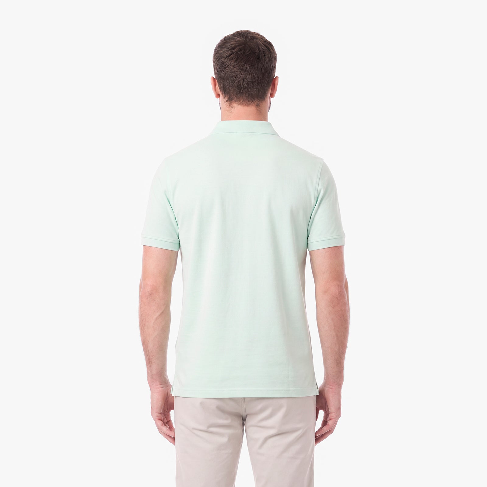 A man viewed from the back wearing a light mint green short-sleeve polo shirt and beige trousers