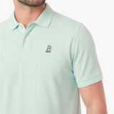 A close-up of a man wearing a light mint green polo shirt with a small embroidered dog logo on the chest