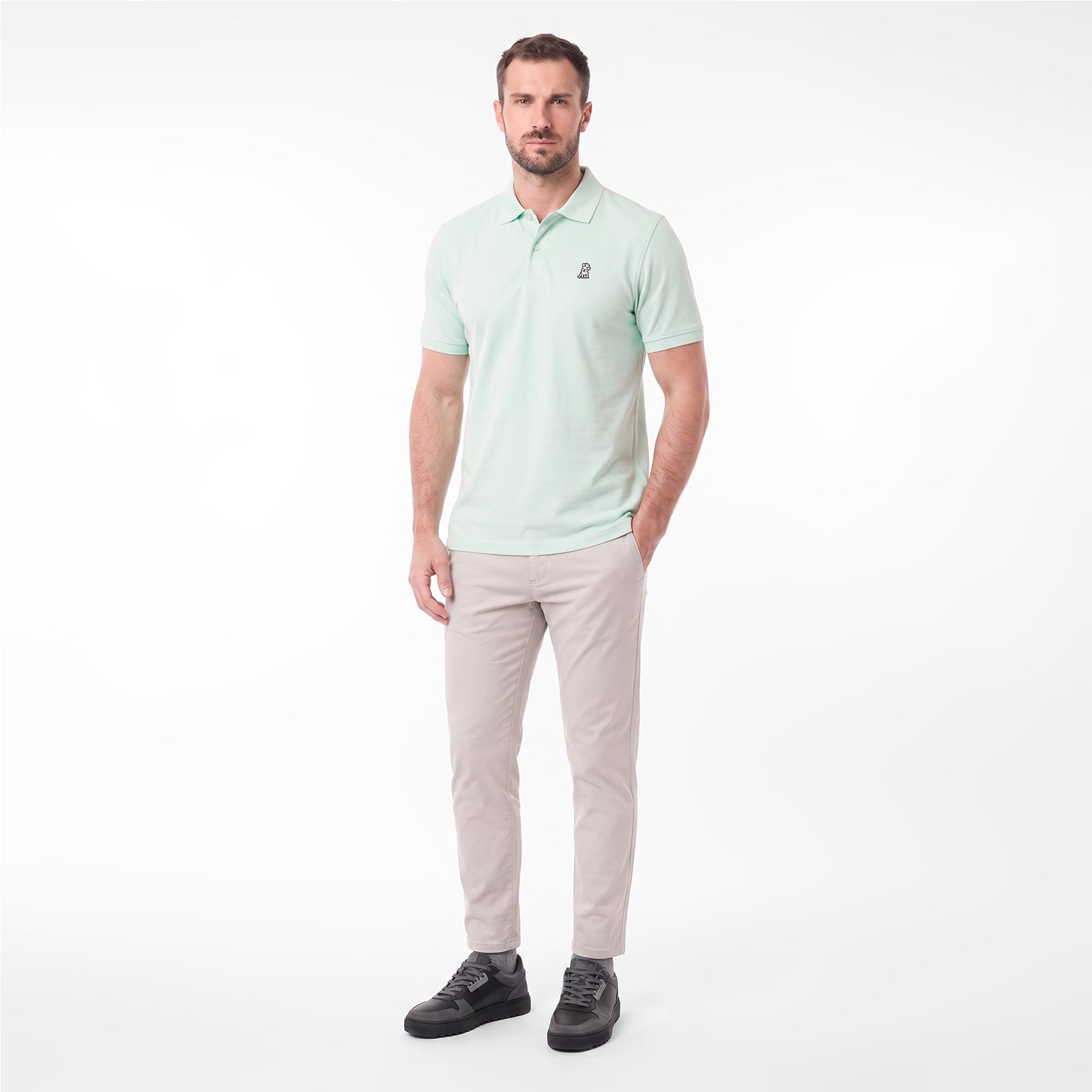 A man modeling a light mint green polo shirt with a small embroidered logo on the chest, paired with beige trousers