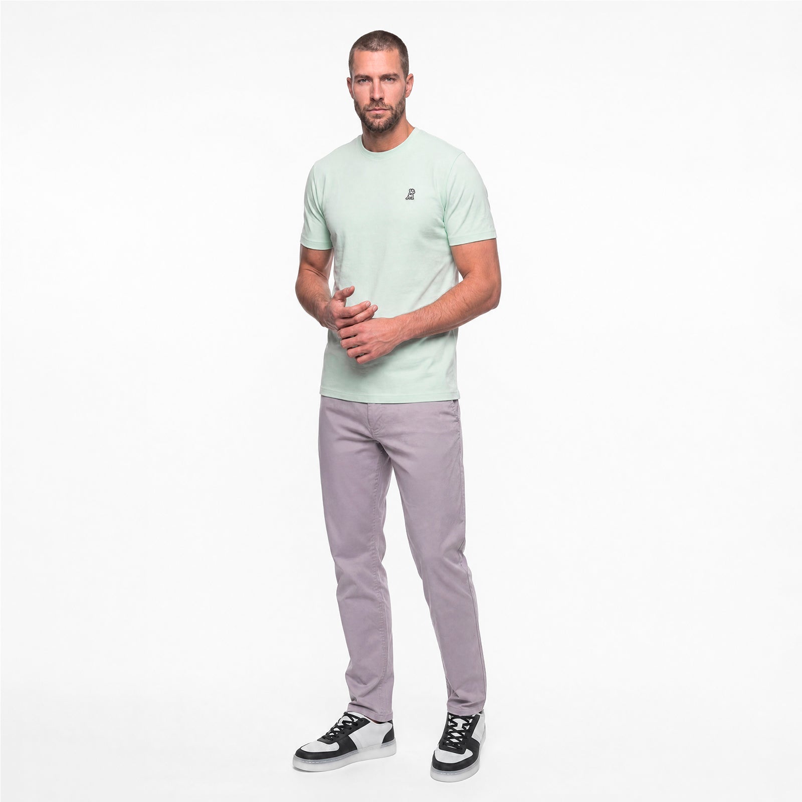 Man wearing a light green t-shirt and gray pants on a white background