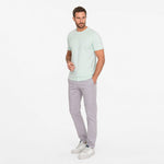Man wearing a light green t-shirt and gray pants on a white background