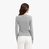 Back view of a woman wearing a gray long-sleeve top and white pants on a white background