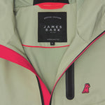 Close-up of the inside of a sage green jacket. A black label reads "SPECIAL EDITION JAMES BARK." The lining is bright pink.