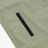 Close-up of the pocket of a sage green jacket. The black zipper pull says "JAMES BARK" in red letters.