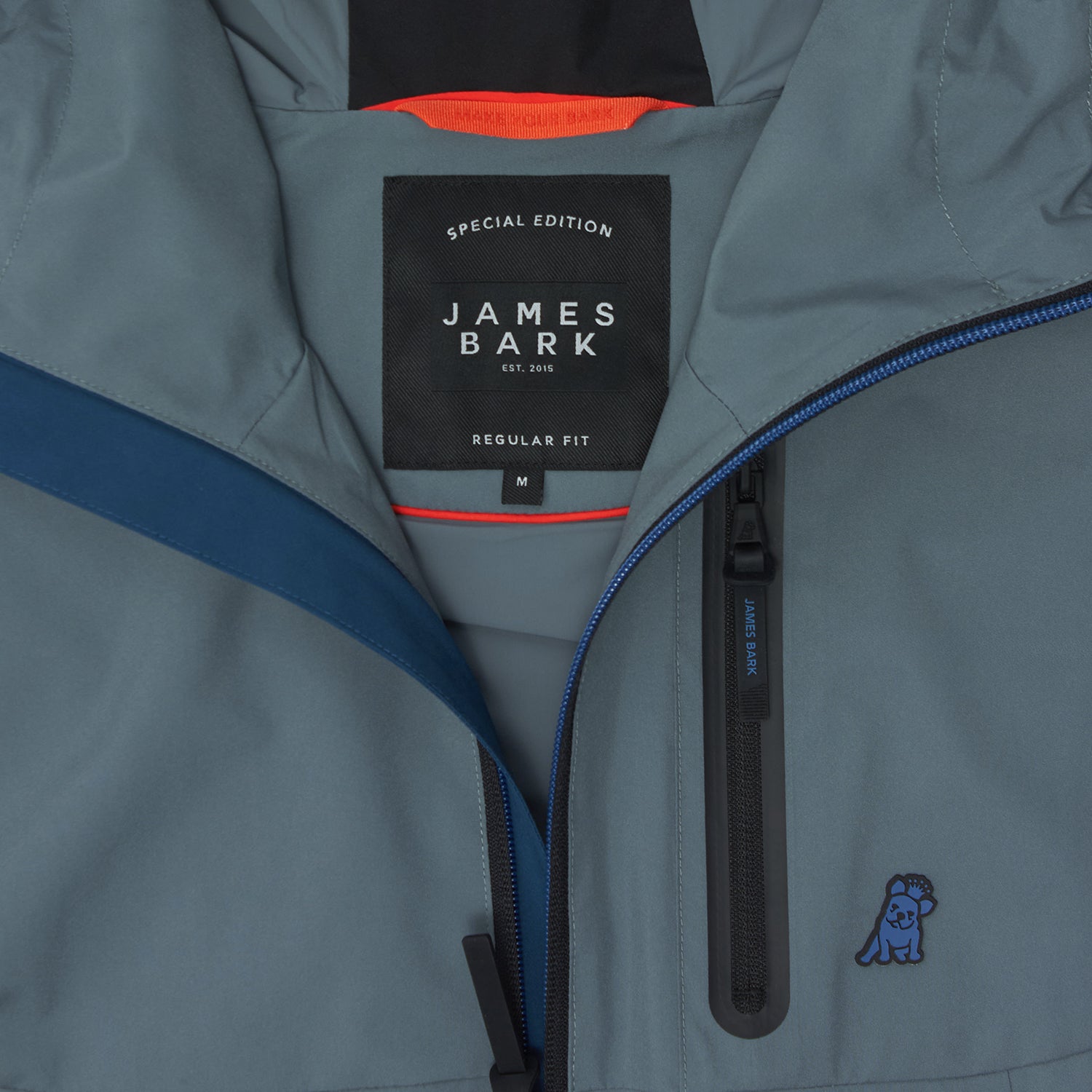 Close-up of the inside of a slate blue jacket. A black label reads "SPECIAL EDITION JAMES BARK". The lining is burnt orange.