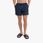 A model from the waist down wearing dark navy blue patterned swim shorts with a drawstring waist and black slide sandals