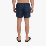 Rear view of a person wearing dark navy patterned shorts and black slide sandals