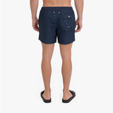 Rear view of a person wearing dark navy patterned shorts and black slide sandals