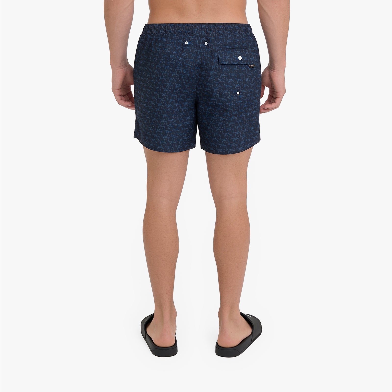 Rear view of a person wearing dark navy patterned shorts and black slide sandals