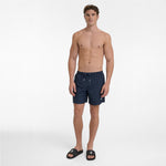 A man wearing dark navy blue patterned swim shorts with a drawstring waist and black slide sandals