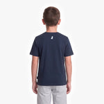 A child viewed from the back wearing a navy blue short-sleeve t-shirt with a small white dog logo on the upper back, paired with light gray pants, against a plain white background.