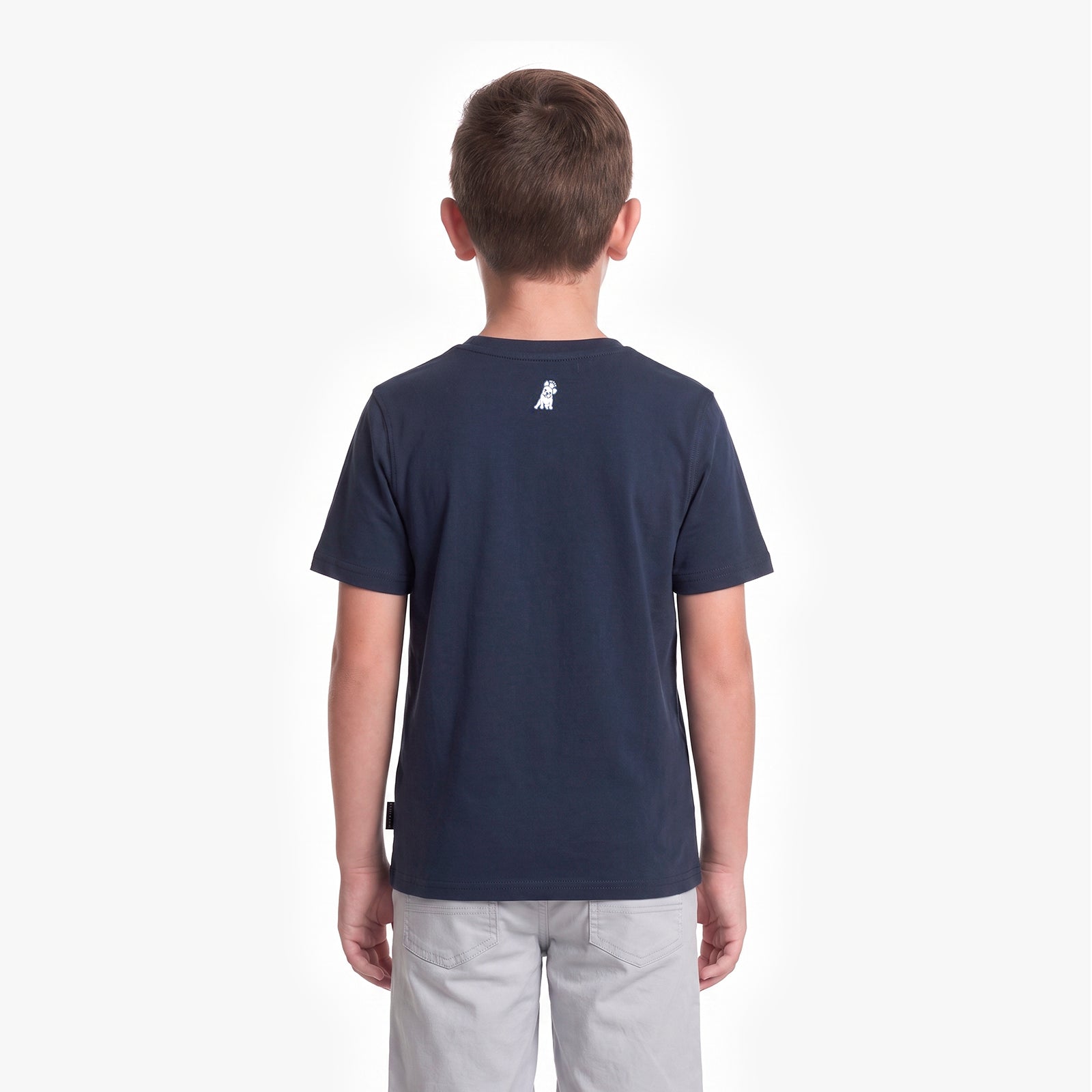 A child viewed from the back wearing a navy blue short-sleeve t-shirt with a small white dog logo on the upper back, paired with light gray pants, against a plain white background.