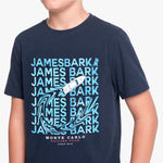 A navy blue short-sleeve t-shirt with a light blue and white graphic print featuring the text 'JAMES BARK' repeated, a sailboat, and 'MONTE CARLO SAILING CLUB SINCE 1915'.
