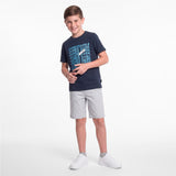 A young boy modeling a dark navy blue t-shirt with a light blue and white 'JAMES BARK' graphic, paired with light gray shorts and white sneakers