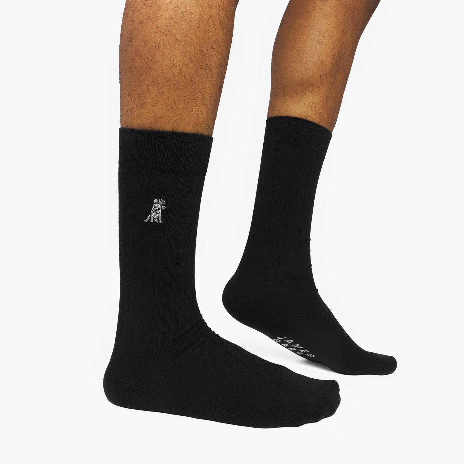 Black socks with a logo on one foot and text on the other, worn by a person on a white background.