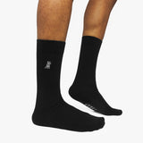 Black socks with a logo on one foot and text on the other, worn by a person on a white background.