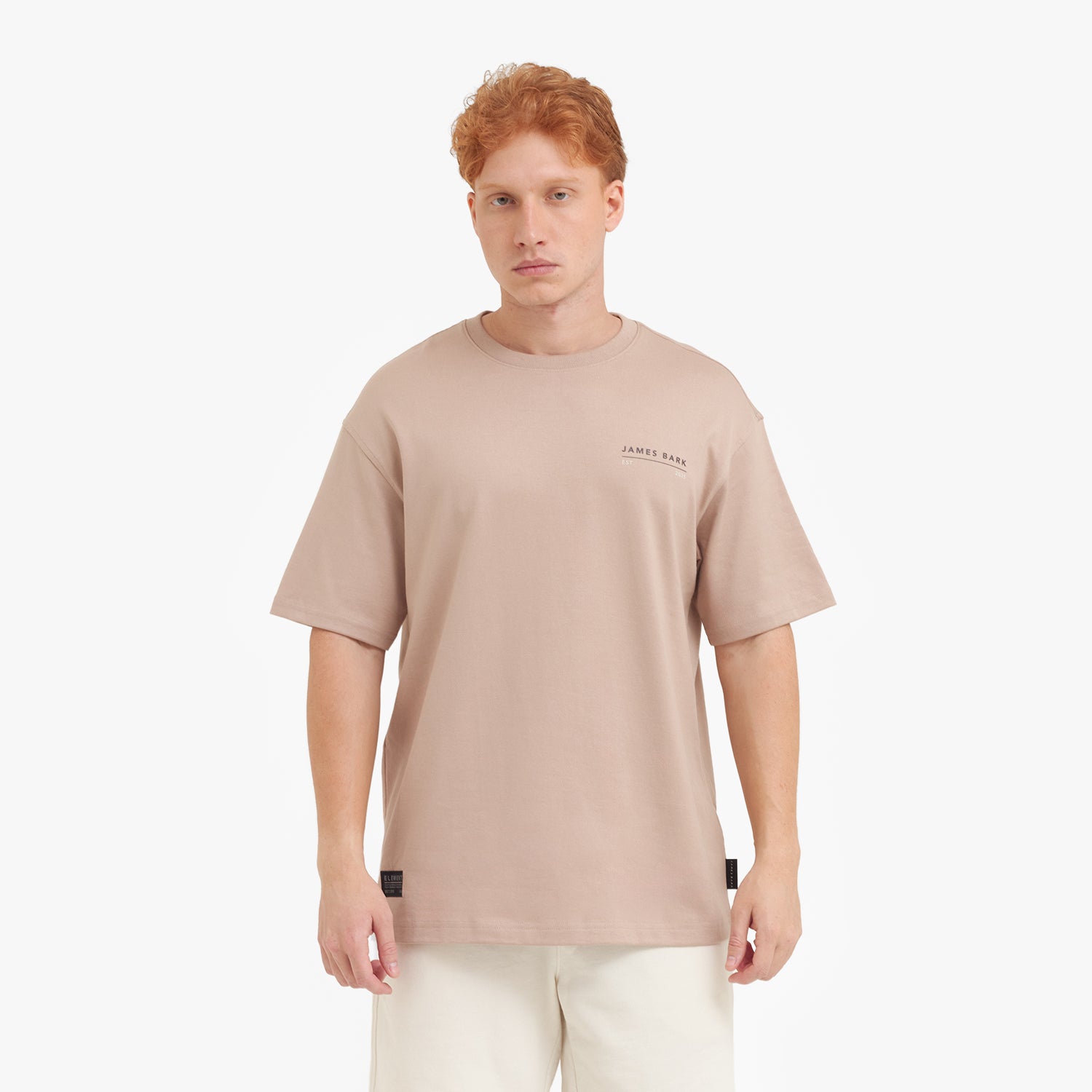 A male model with red hair wearing a beige oversized t-shirt, shown from the chest up.