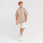 Full-body shot of a male model wearing a beige t-shirt, off-white shorts, and white sneakers