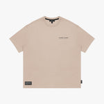 Front view of a beige t-shirt laid flat, showing a small logo on the chest and a black tag on the hem