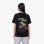 A woman viewed from the back, wearing a black graphic t-shirt with a large James Bark design and light blue jeans