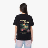 A woman viewed from the back, wearing a black graphic t-shirt with a large James Bark design and light blue jeans