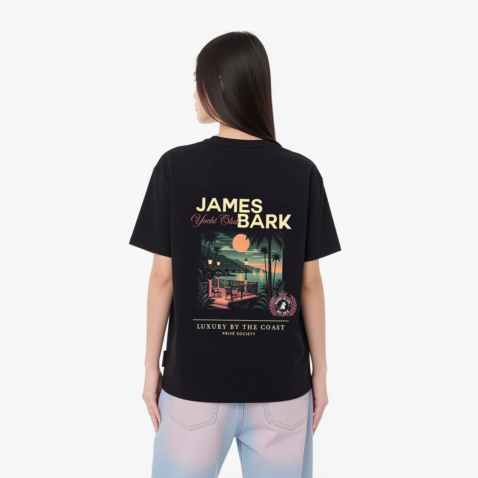 A woman viewed from the back, wearing a black graphic t-shirt with a large James Bark design and light blue jeans