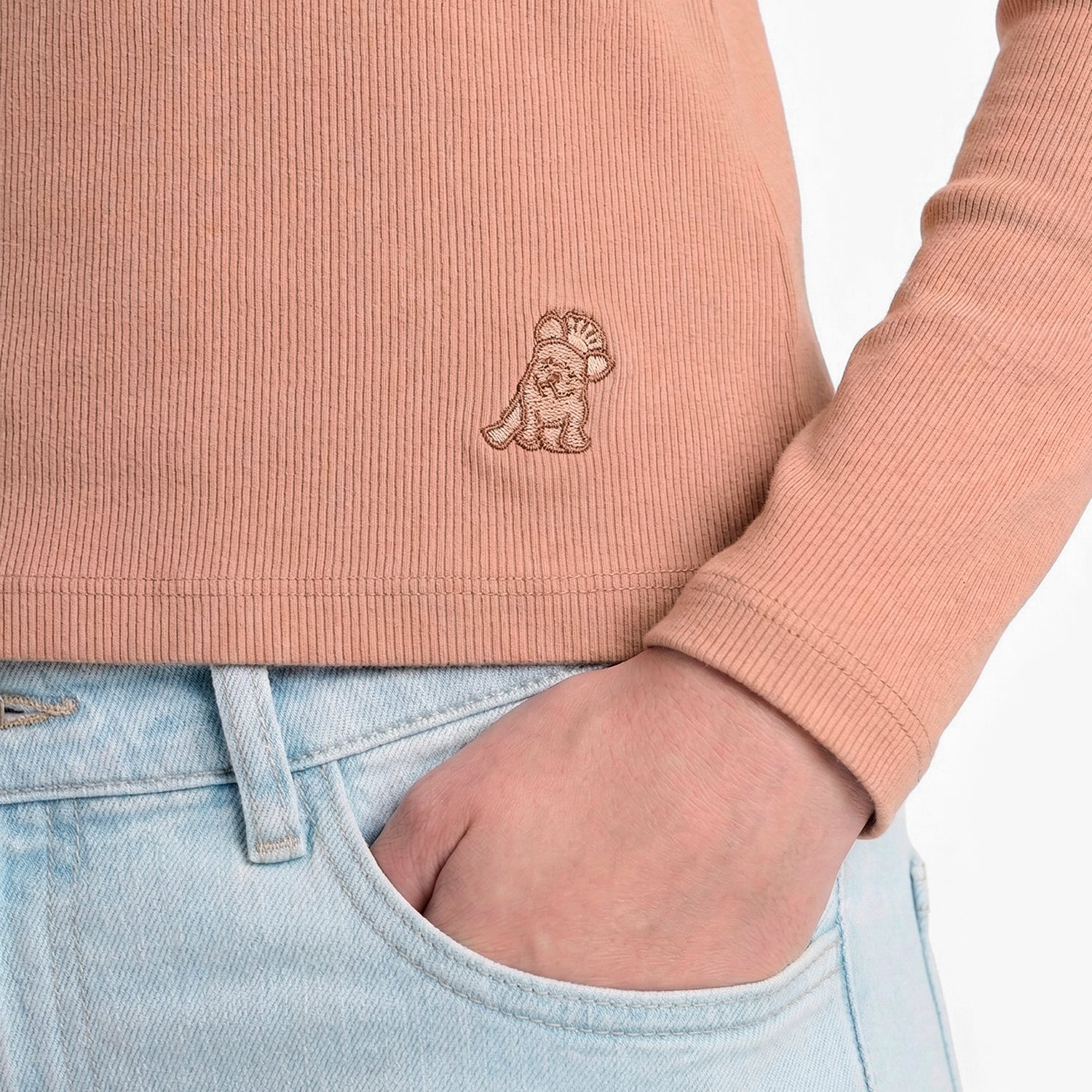 Person wearing a pink ribbed sweater with a logo and light blue jeans.