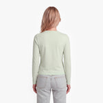 Woman wearing a light green long-sleeve shirt and light gray jeans on a white background