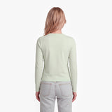 Woman wearing a light green long-sleeve shirt and light gray jeans on a white background