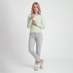 Woman wearing a light green sweater and gray jeans on a white background