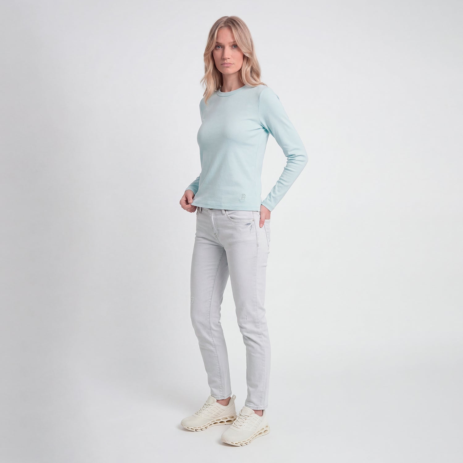Woman wearing a light blue long-sleeve top and light gray jeans on a white background