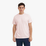Man wearing a light pink t-shirt and dark pants on a white background