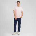 Man wearing a light pink t-shirt and dark blue pants on a gray background