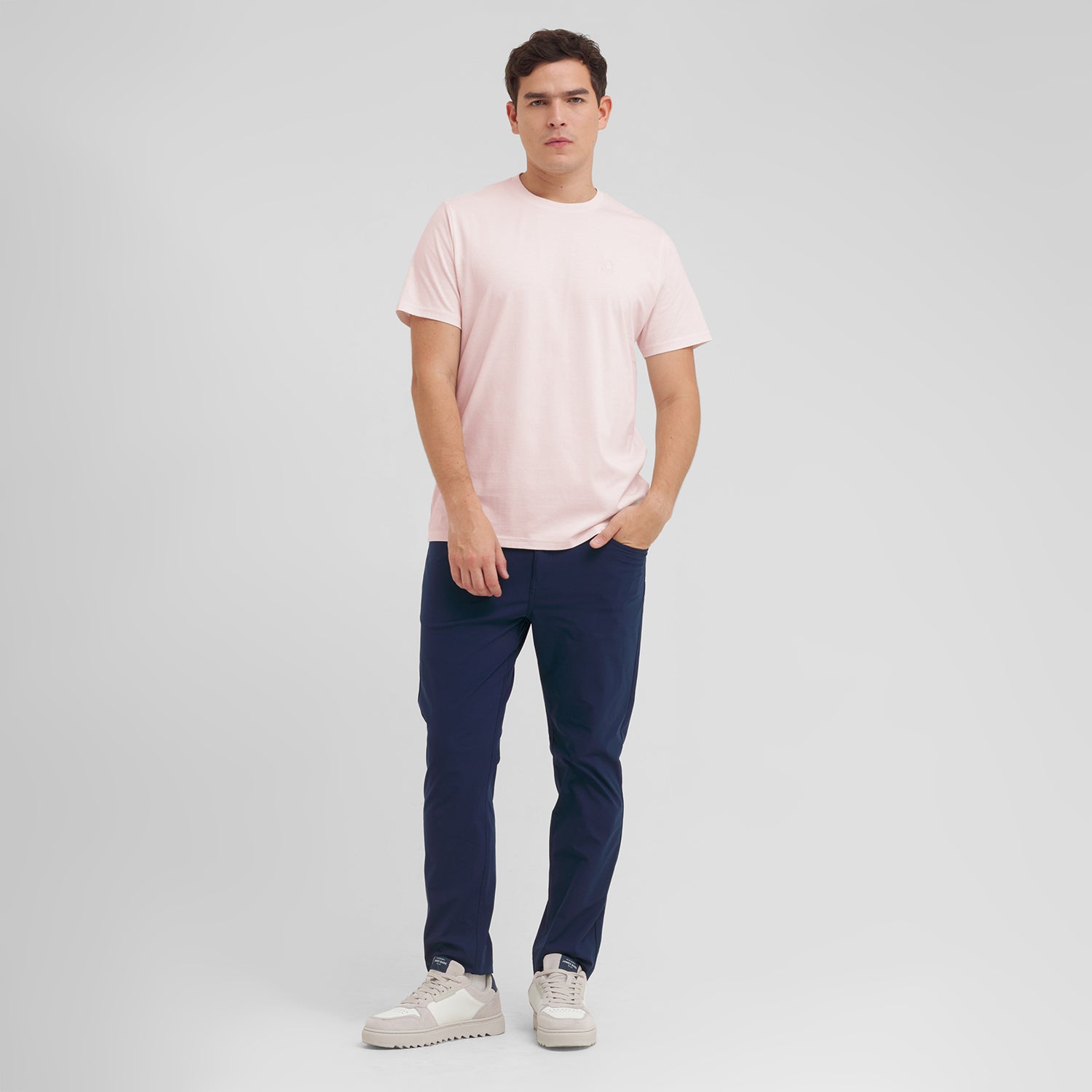 Man wearing a light pink t-shirt and dark blue pants on a gray background