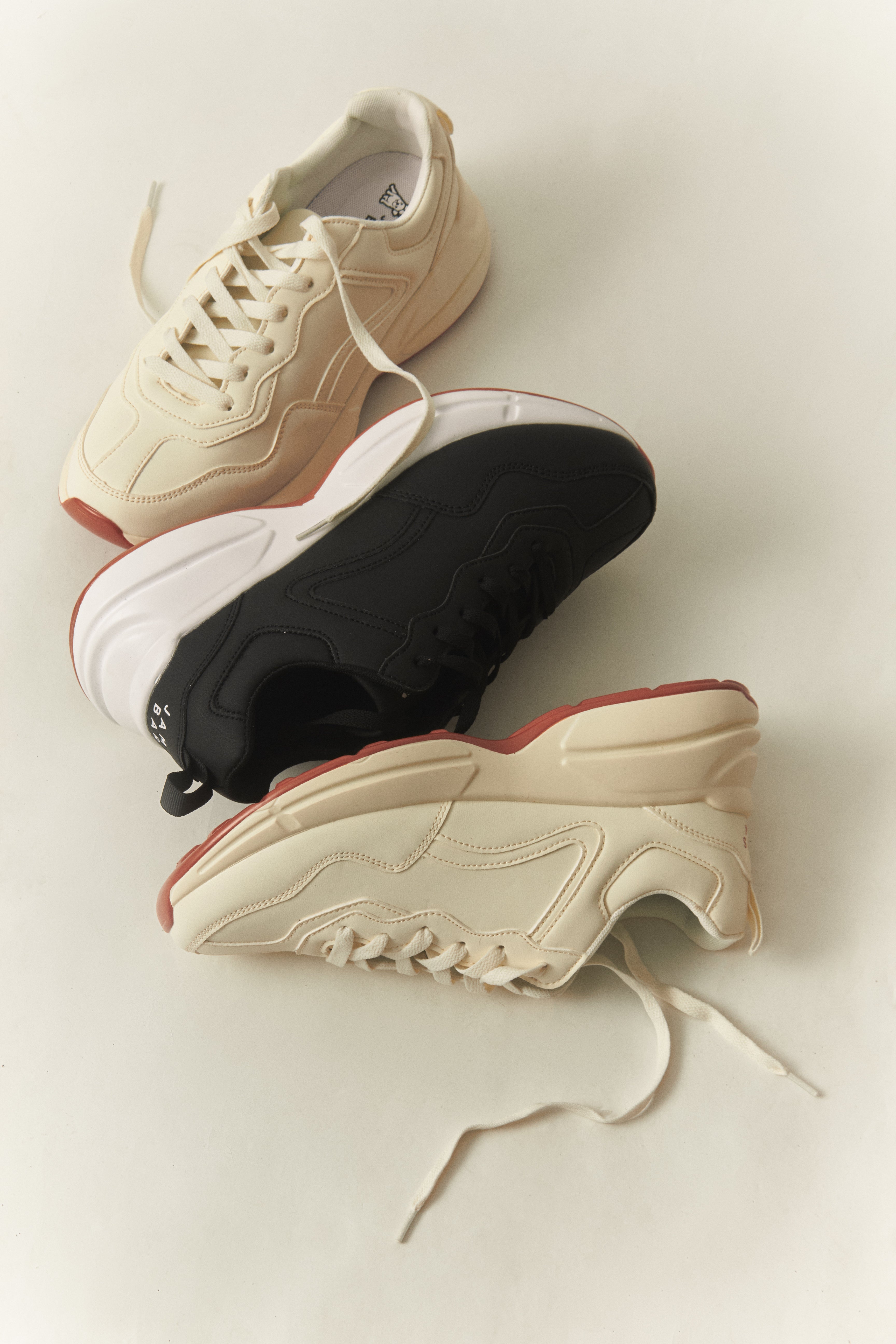 Three pairs of sneakers in beige, black, and white on a light background