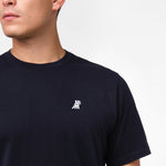 Person wearing a navy blue t-shirt with a small white logo on a plain background