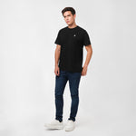 Man wearing a black t-shirt, blue jeans, and white sneakers on a white background
