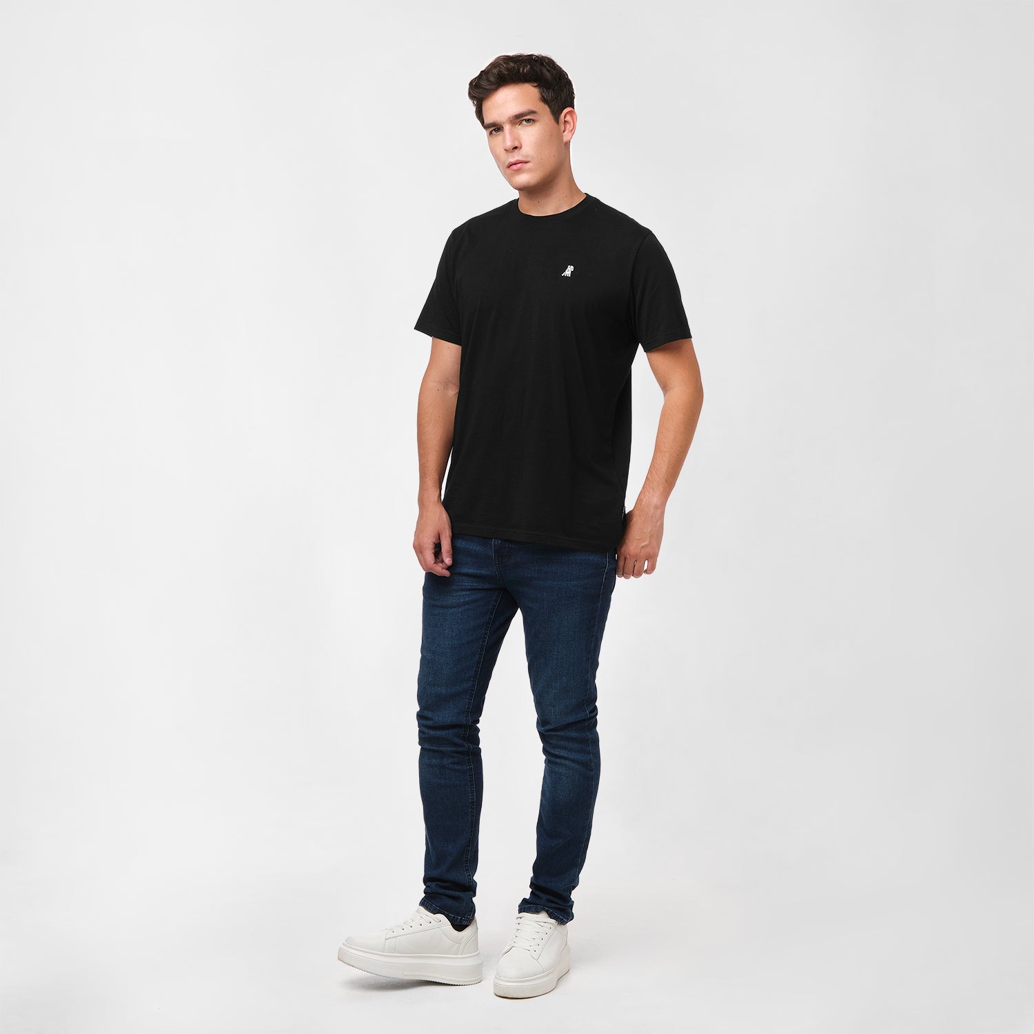 Man wearing a black t-shirt, blue jeans, and white sneakers on a white background
