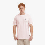 Man wearing a light pink t-shirt with a small logo on a white background