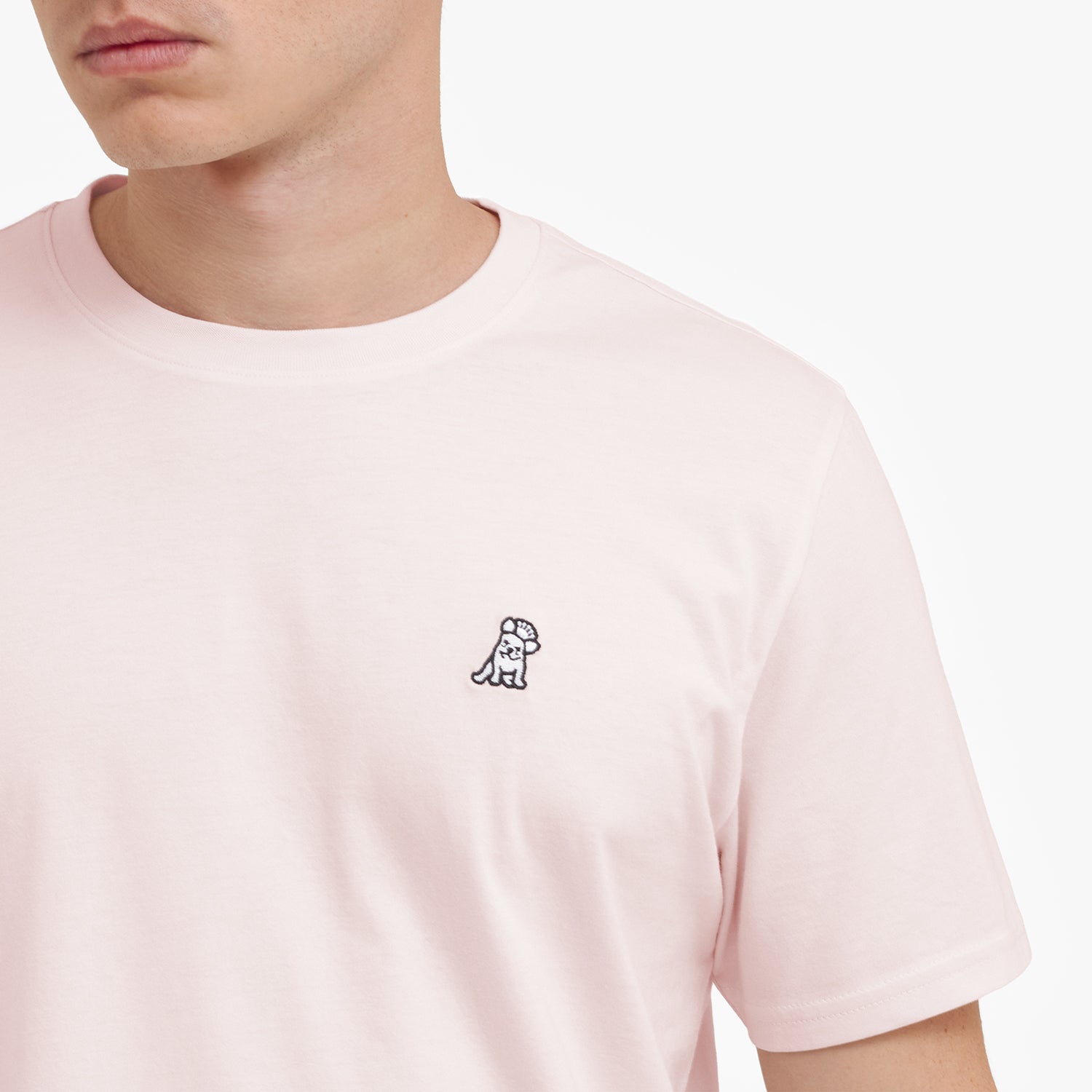 Close-up of a person wearing a light pink t-shirt with a small logo on the chest.